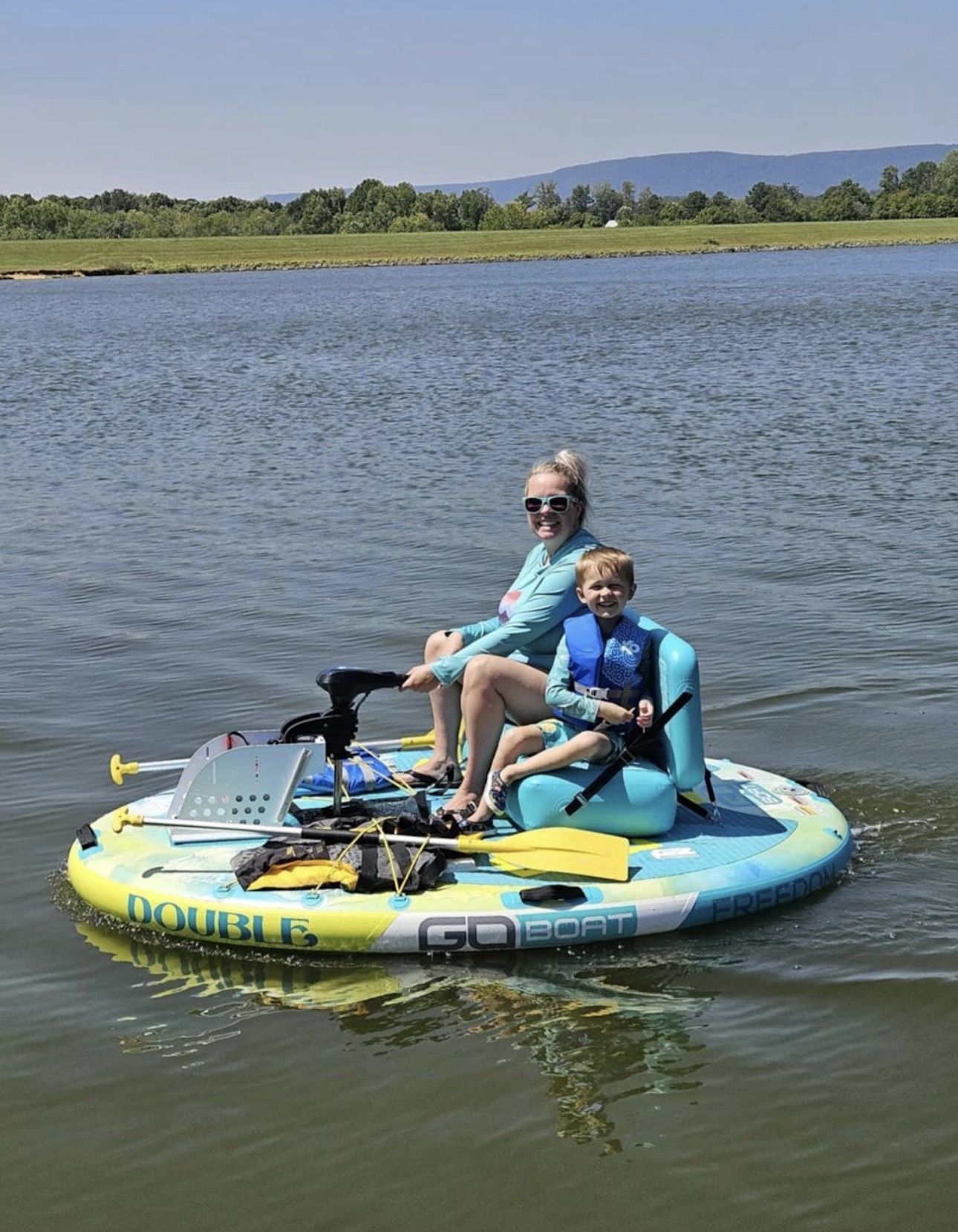 A mother and her young son smiling while riding a yellow and aqua Double GoBoat on calm water