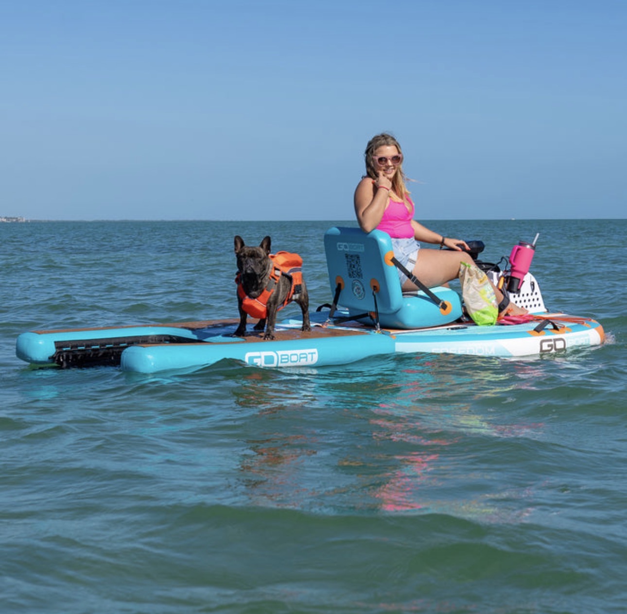 A woman and her dog in an orange life vest riding an aqua GoBoat across open Gulf water